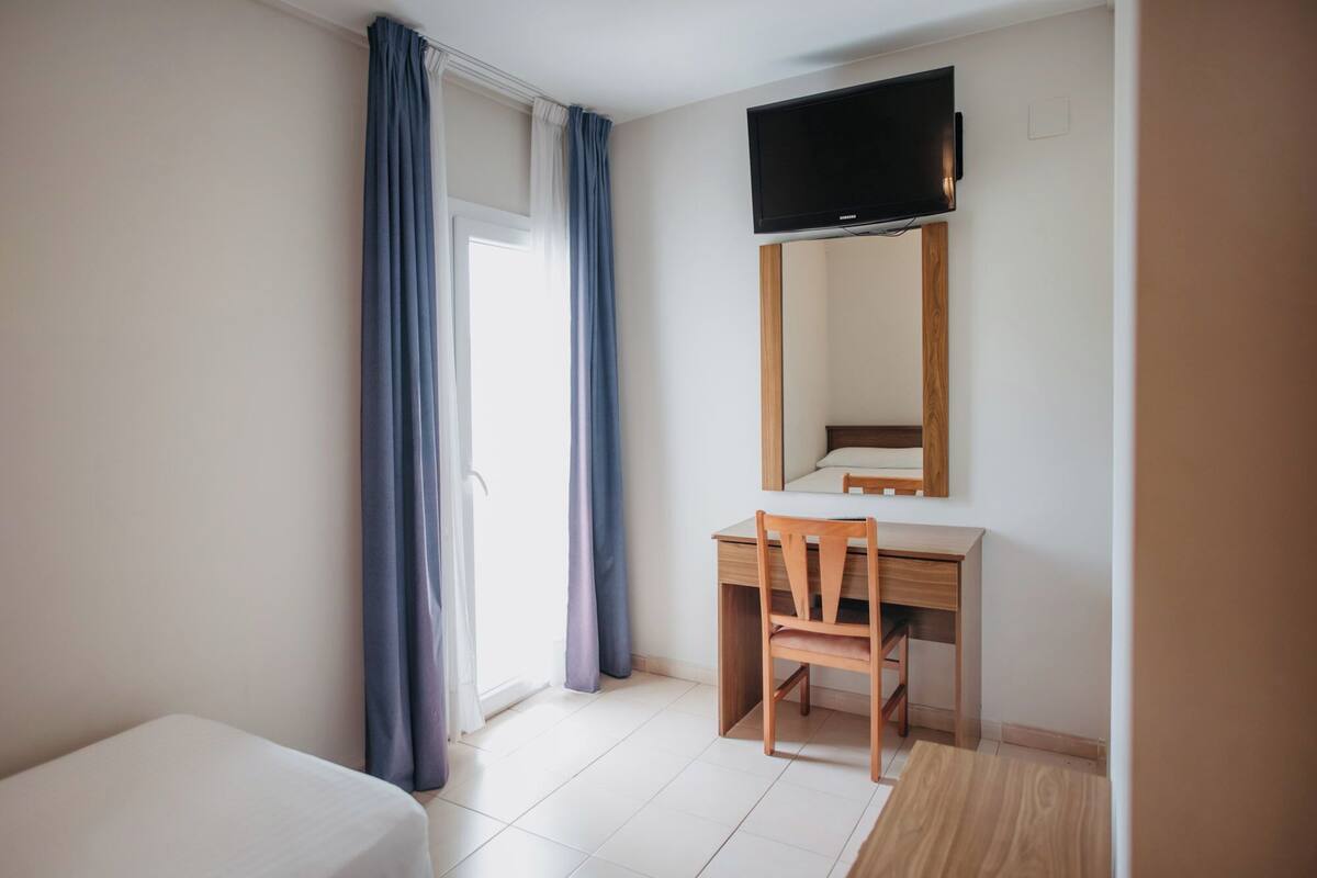 A hotel room with a bed, a desk, a chair, a flat-screen TV, and a large mirror.