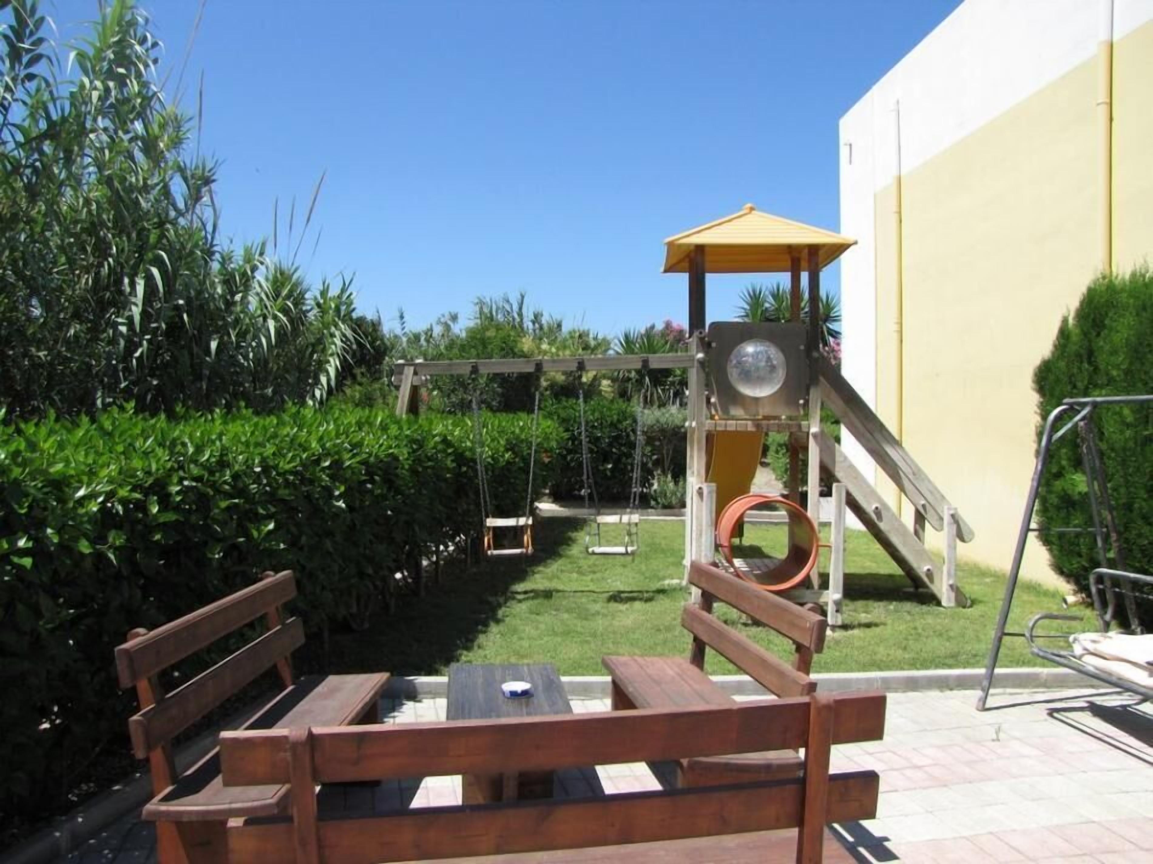 A wooden bench, a swing set, and a small play structure with a slide and a climbing ladder.