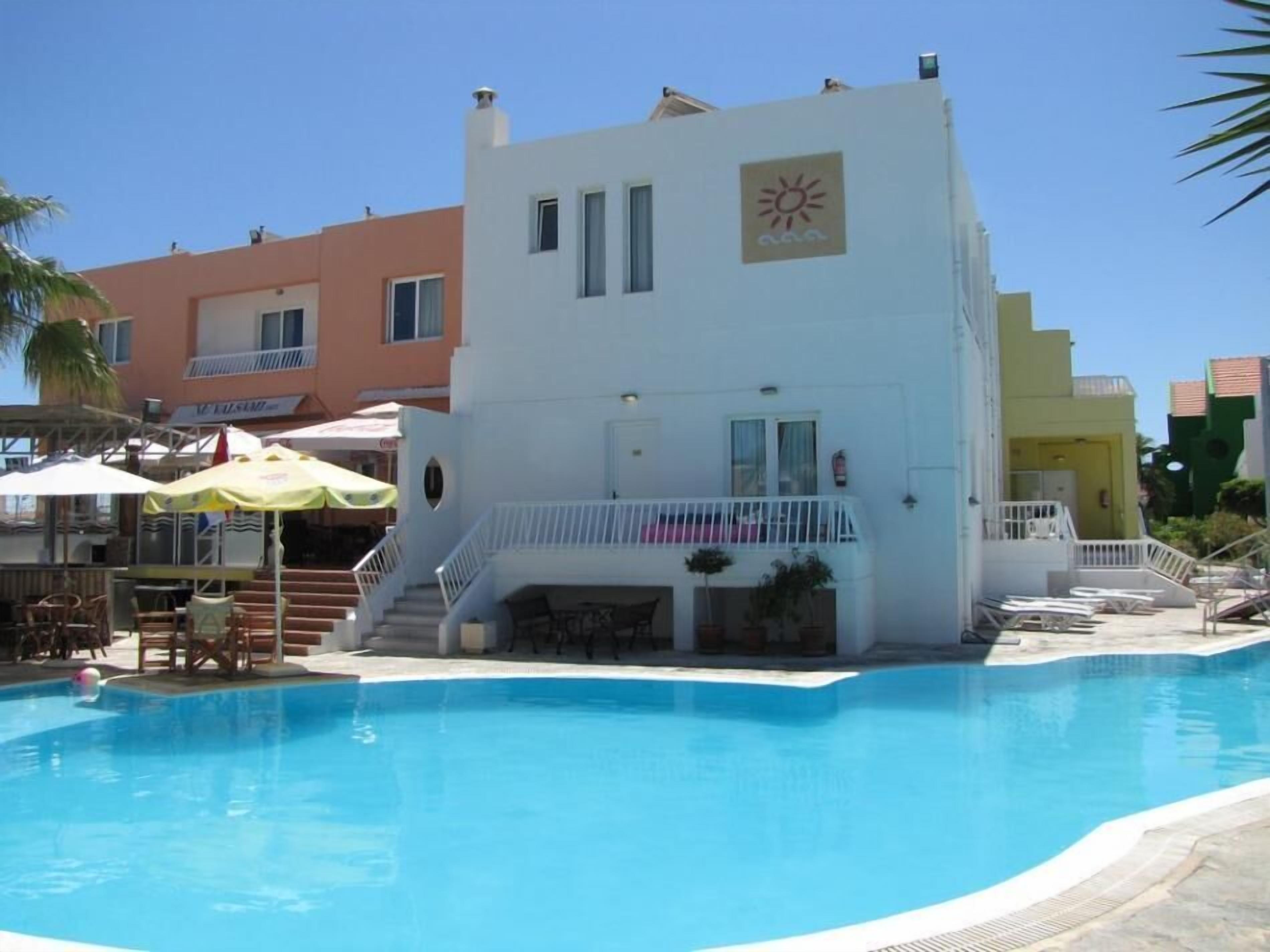 A modern building with a pool, featuring a sun symbol on the facade, a balcony, and a staircase leading to the entrance.