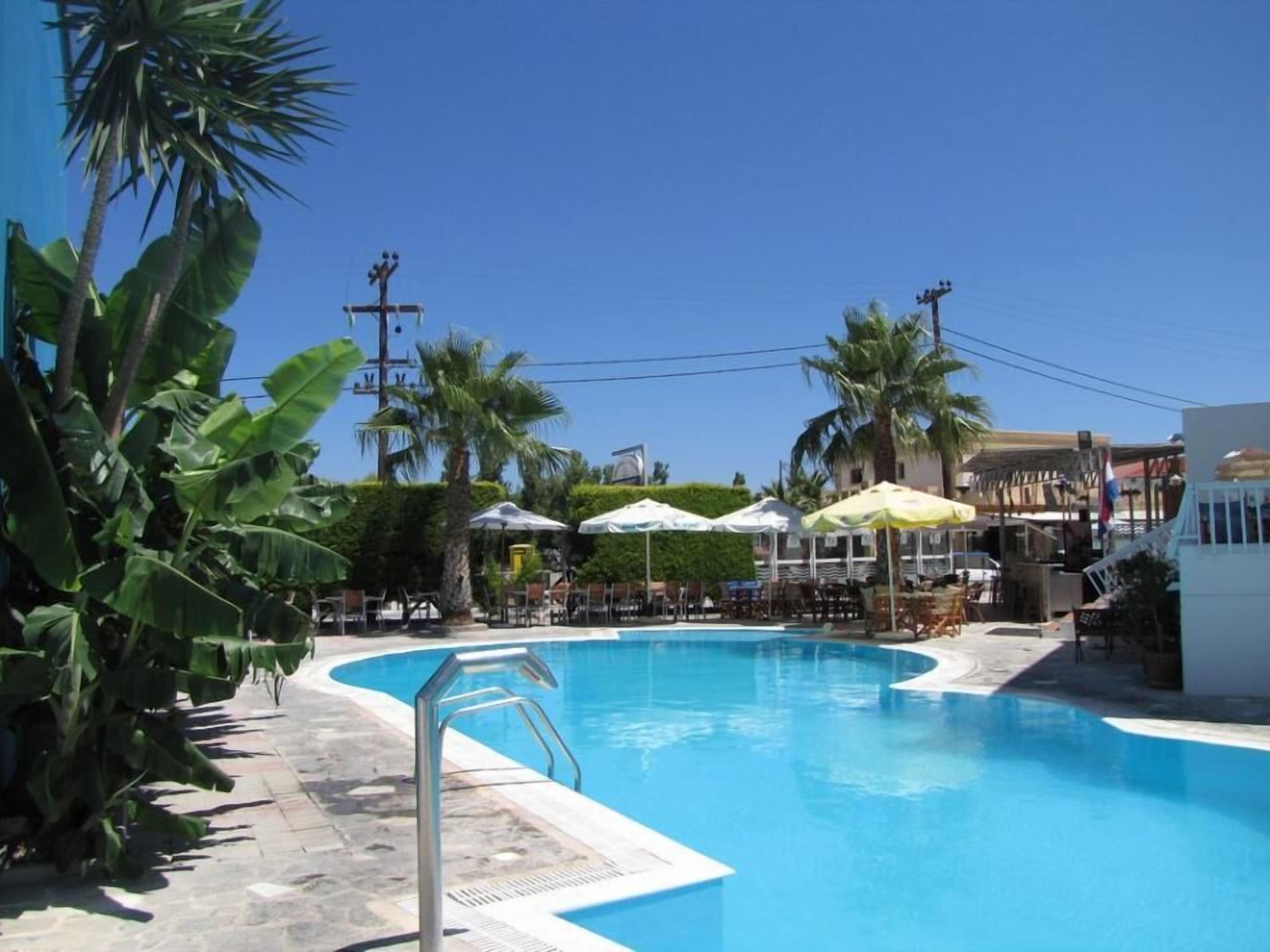 Una piscina con sillas de descanso y sombrillas, rodeada de palmeras y edificios.