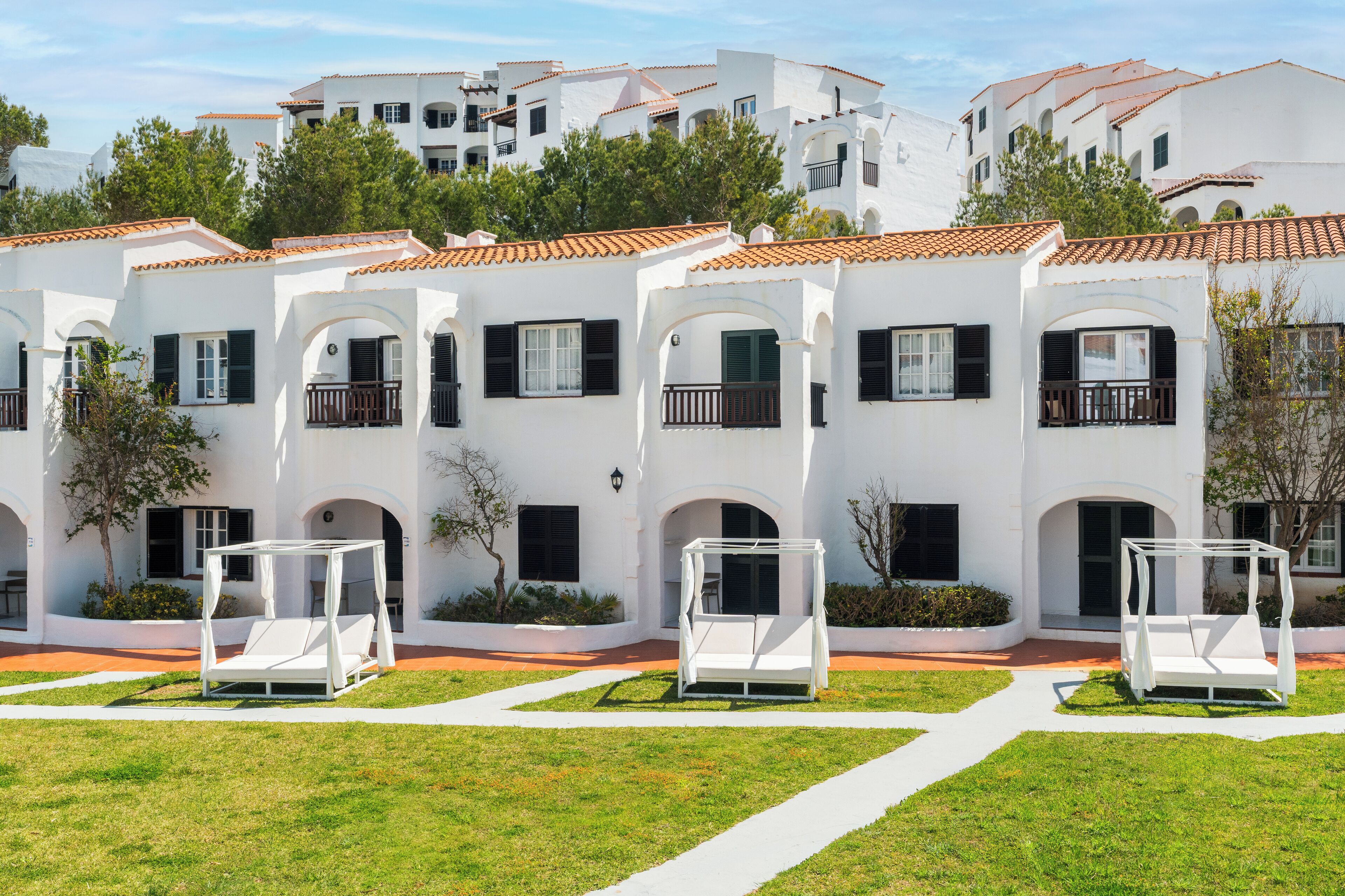 Un edificio blanco con balcones y un jardín con macetas blancas.