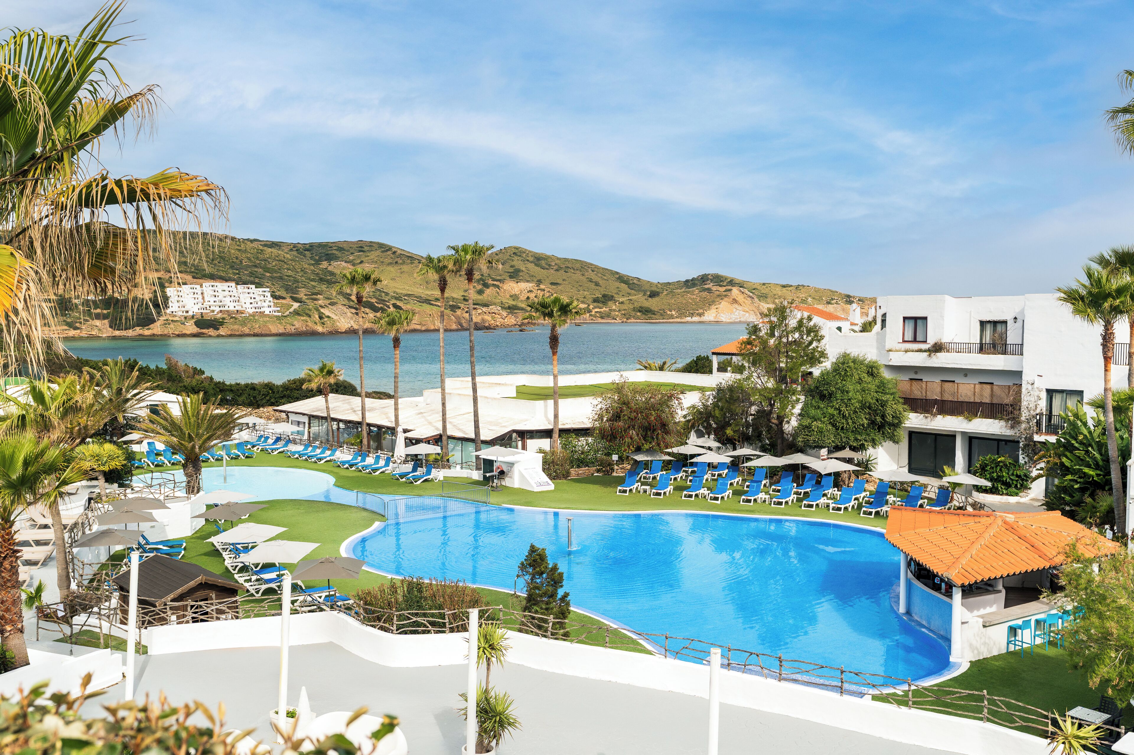 Un resort con una amplia piscina, tumbonas y vistas al mar.