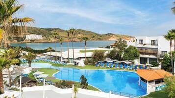 Un resort con una amplia piscina, tumbonas y vistas al mar.