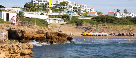 A coastal area with rocky terrain, a beach, and a building complex with multiple balconies.