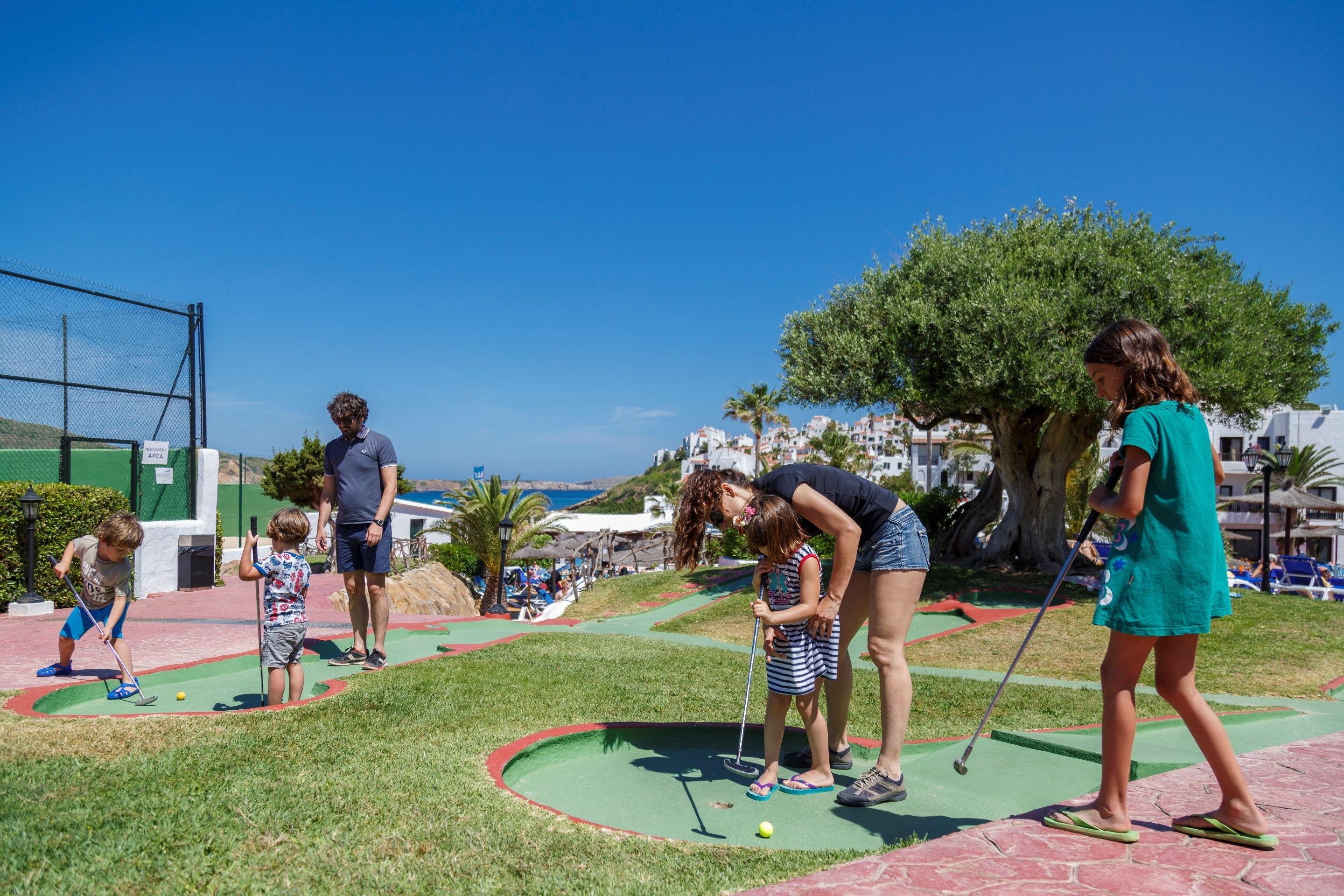 A miniature golf course with a clear view of the sea and buildings in the background.