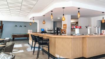 Zona de bar moderna con mostrador de madera, taburetes negros y luces colgantes.