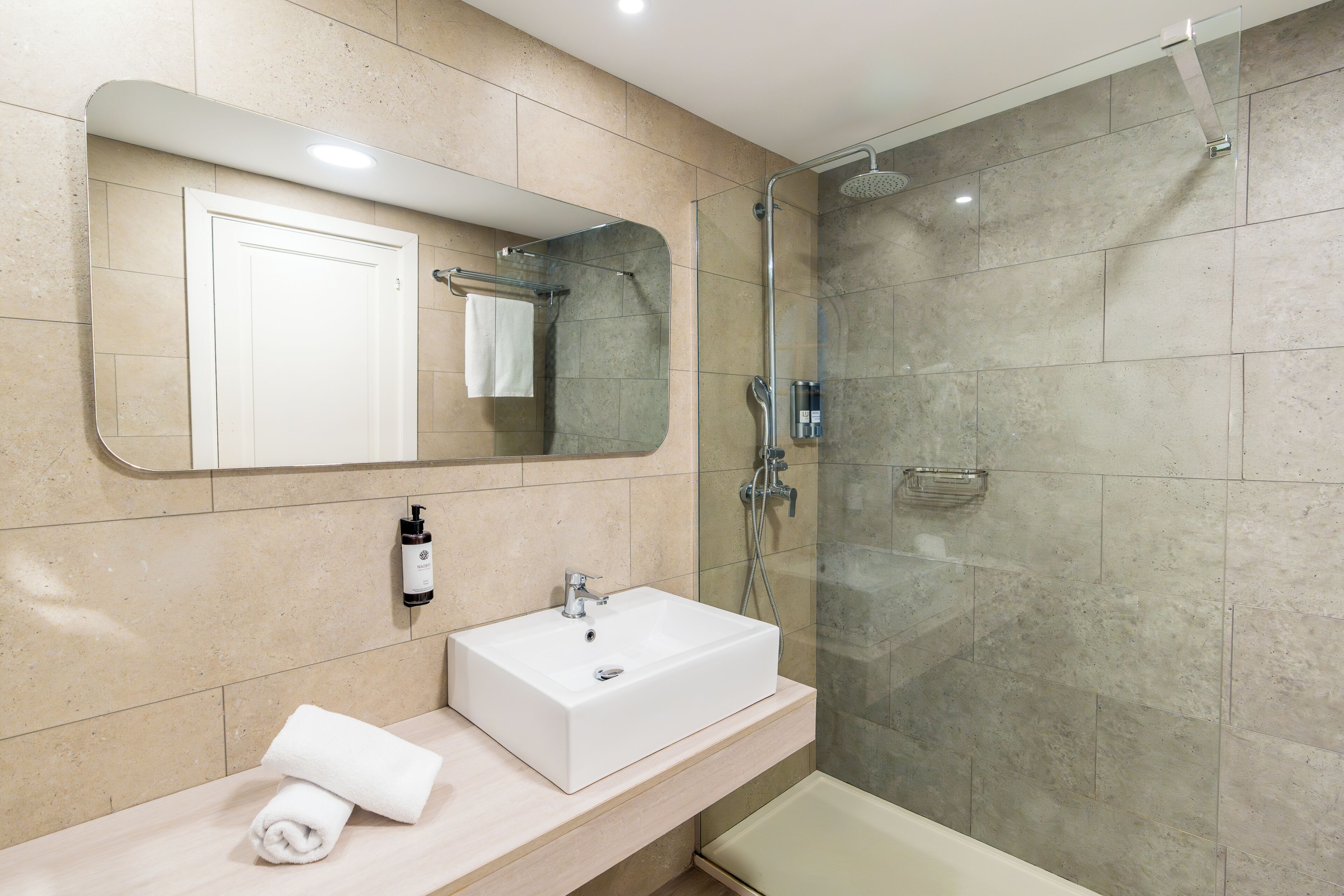 Une salle de bain moderne avec un grand miroir, un lavabo blanc, une douchette à main et une douche à parois de verre.