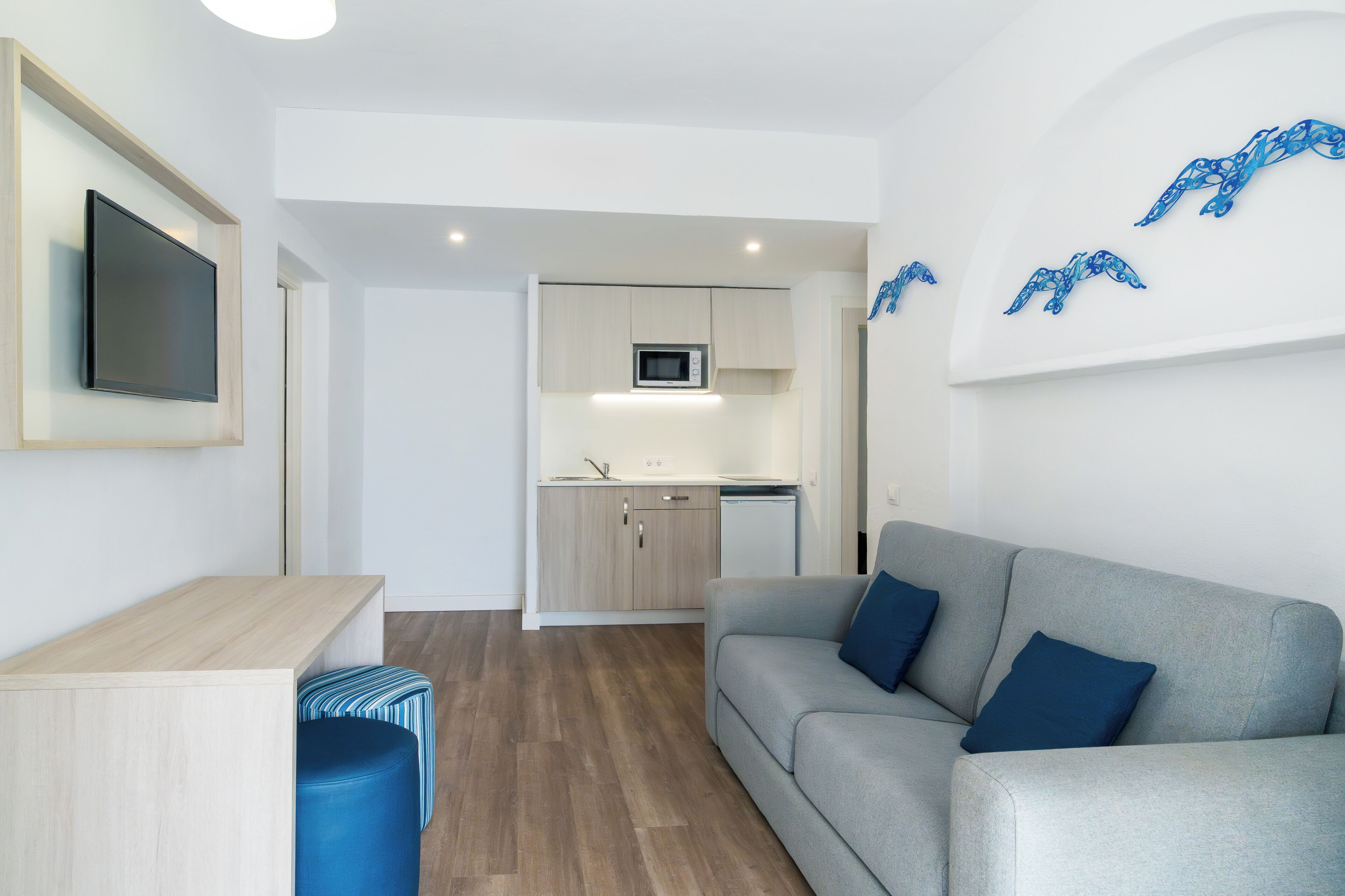 A modern living room with a grey sofa, a wooden coffee table, and a blue ottoman.