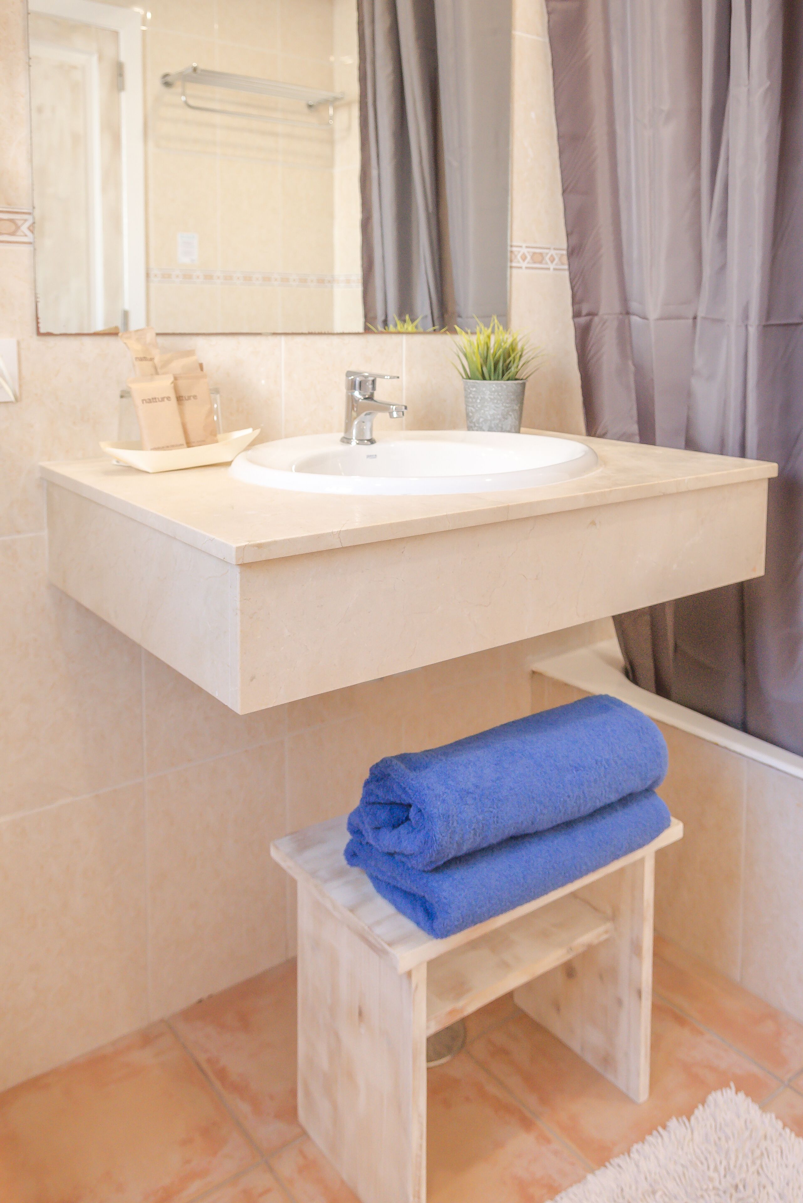 A bathroom with a sink, mirror, towel rack, and a small wooden stool.