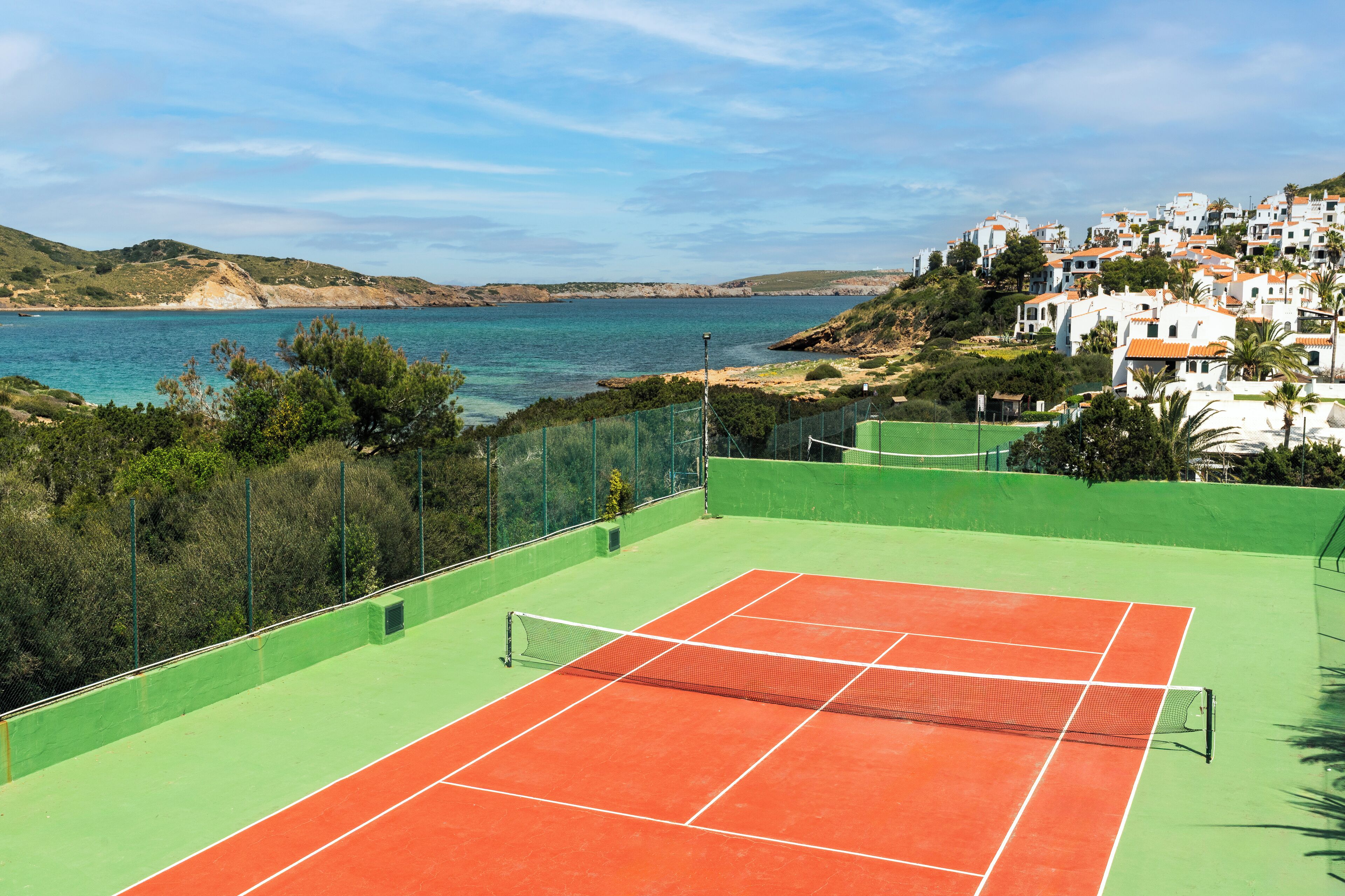 Ein Tennisplatz mit Netz, umgeben von Grün und Blick auf die Küste.