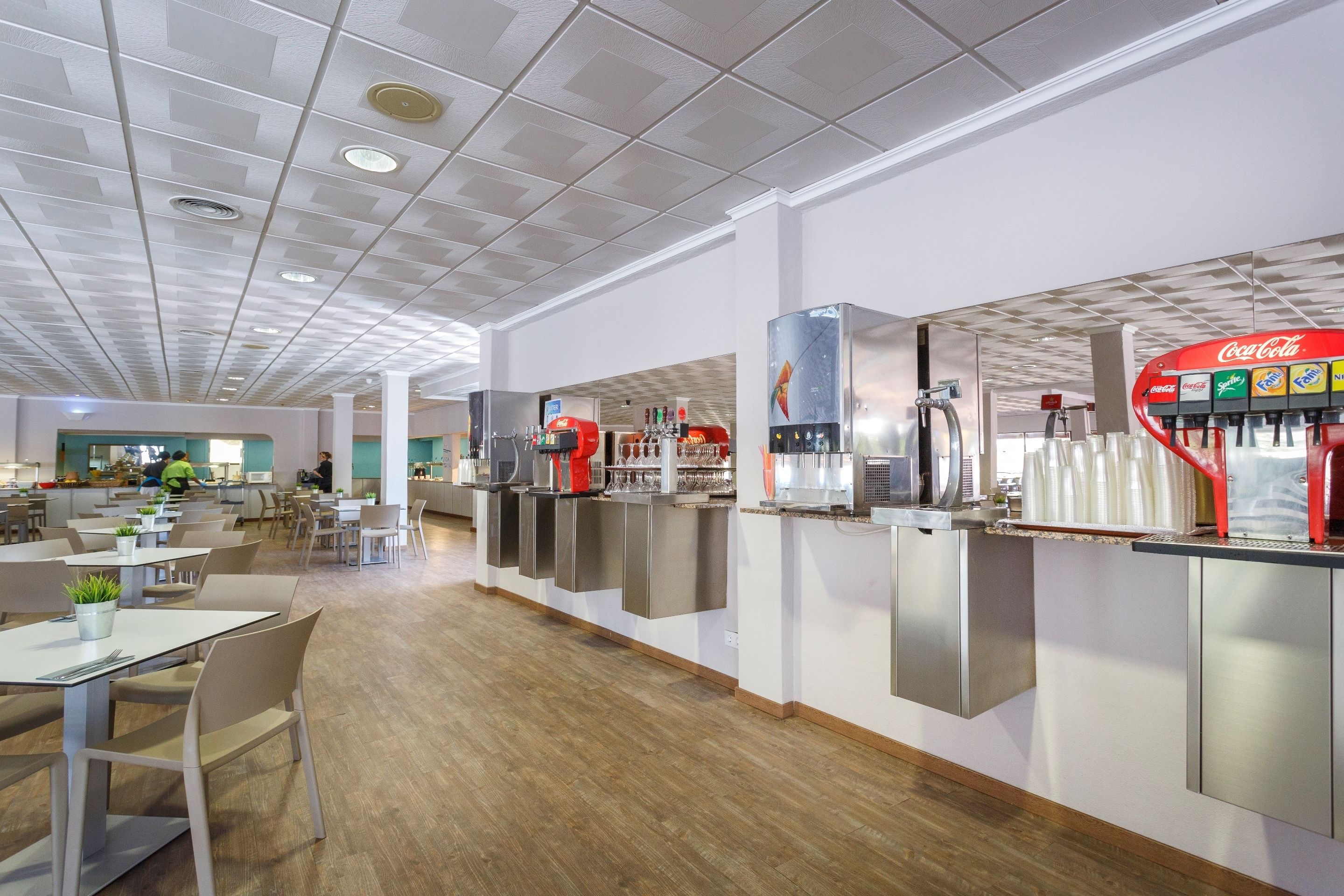 Una cafetería moderna con mostradores de acero inoxidable, una máquina expendedora de Coca-Cola y zonas de estar.