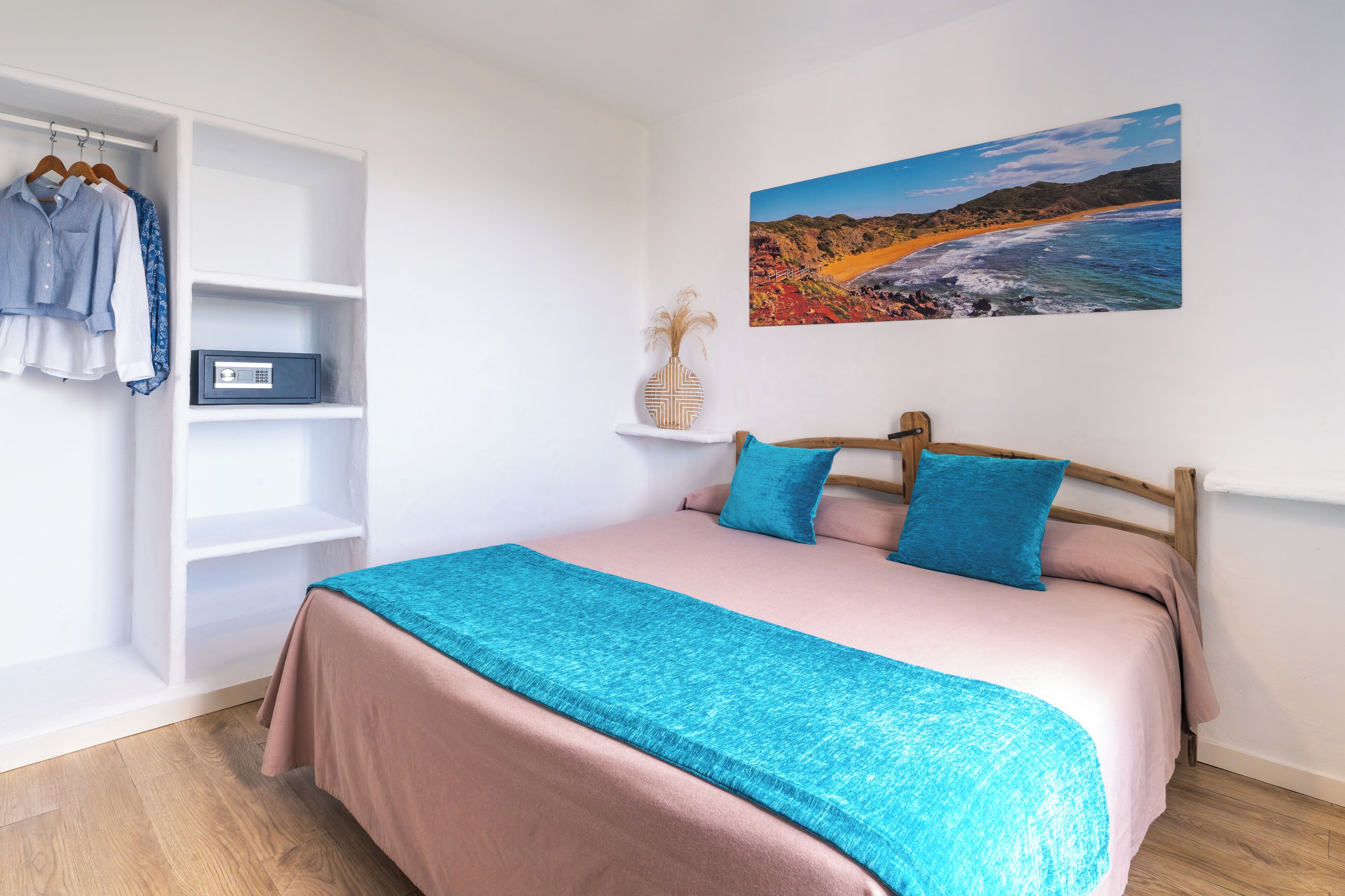 A bedroom with a bed, a wardrobe, a shelf with a vase, and a painting on the wall.