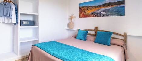 A bedroom with a bed, a wardrobe, a shelf with a vase, and a painting on the wall.