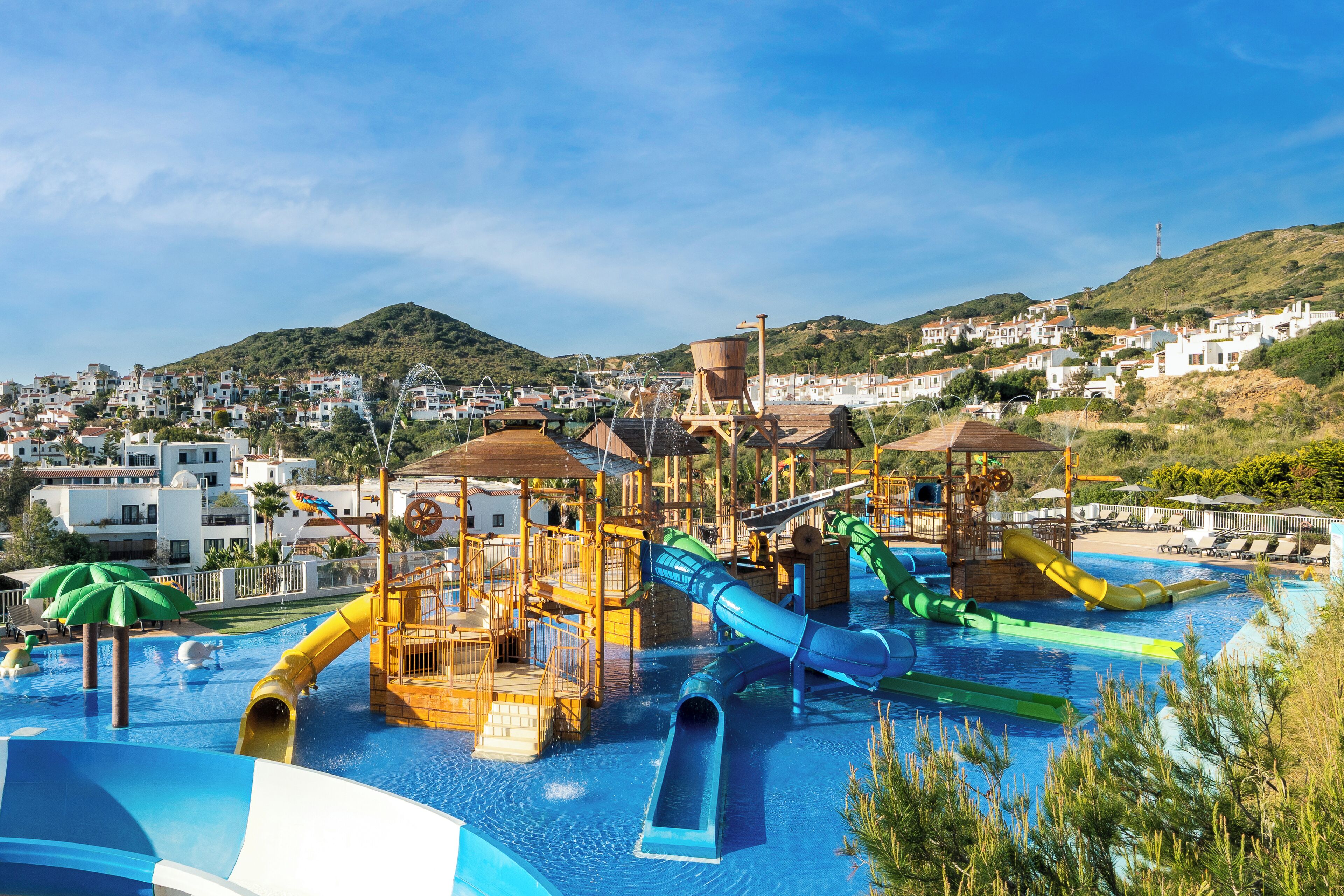 Een waterpark met glijbanen en zwembaden, omringd door heuvels en witte gebouwen.