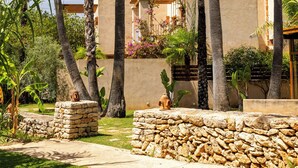 A courtyard with palm trees, a stone wall, and a building with balconies. - Can Lluc Boutique Country Hotel & Villas (Sant Antoni de Portmany)