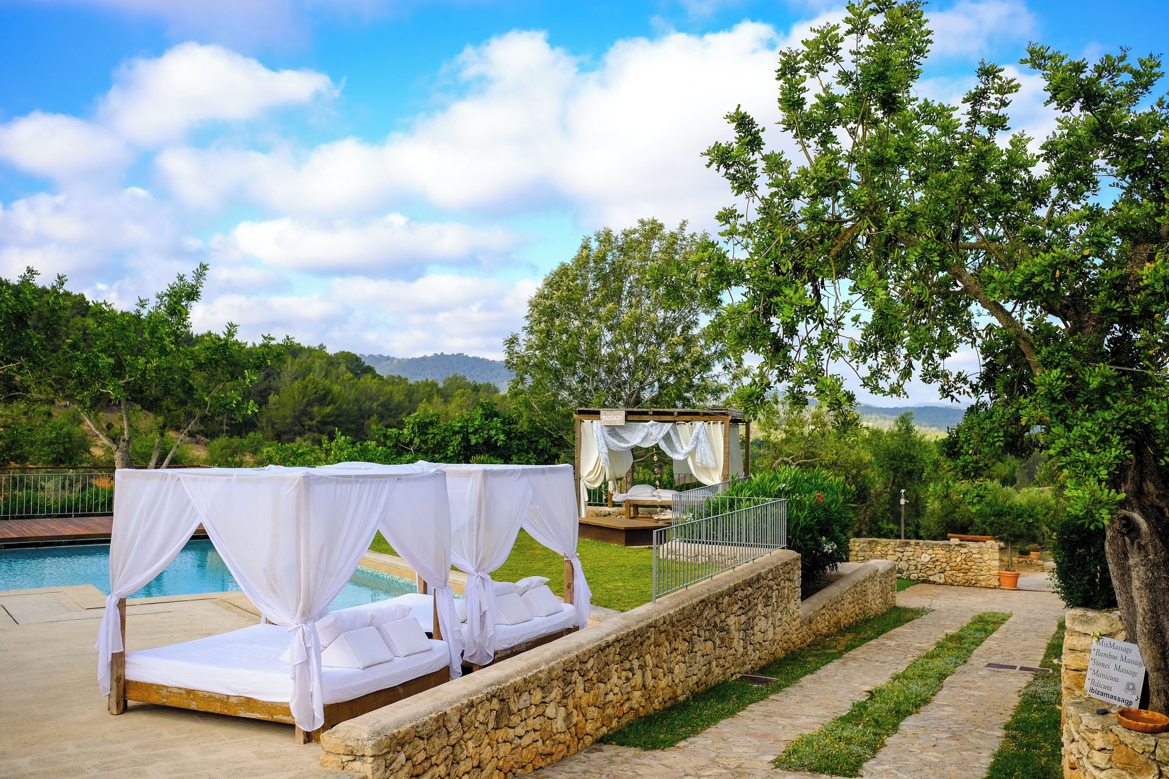 A poolside bed with a canopy, a wooden deck, and a stone wall.