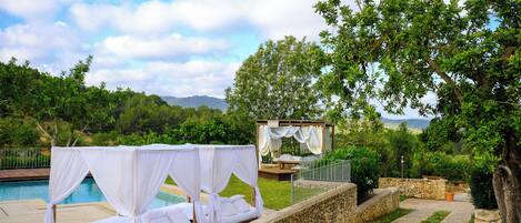 A poolside bed with a canopy, a wooden deck, and a stone wall.