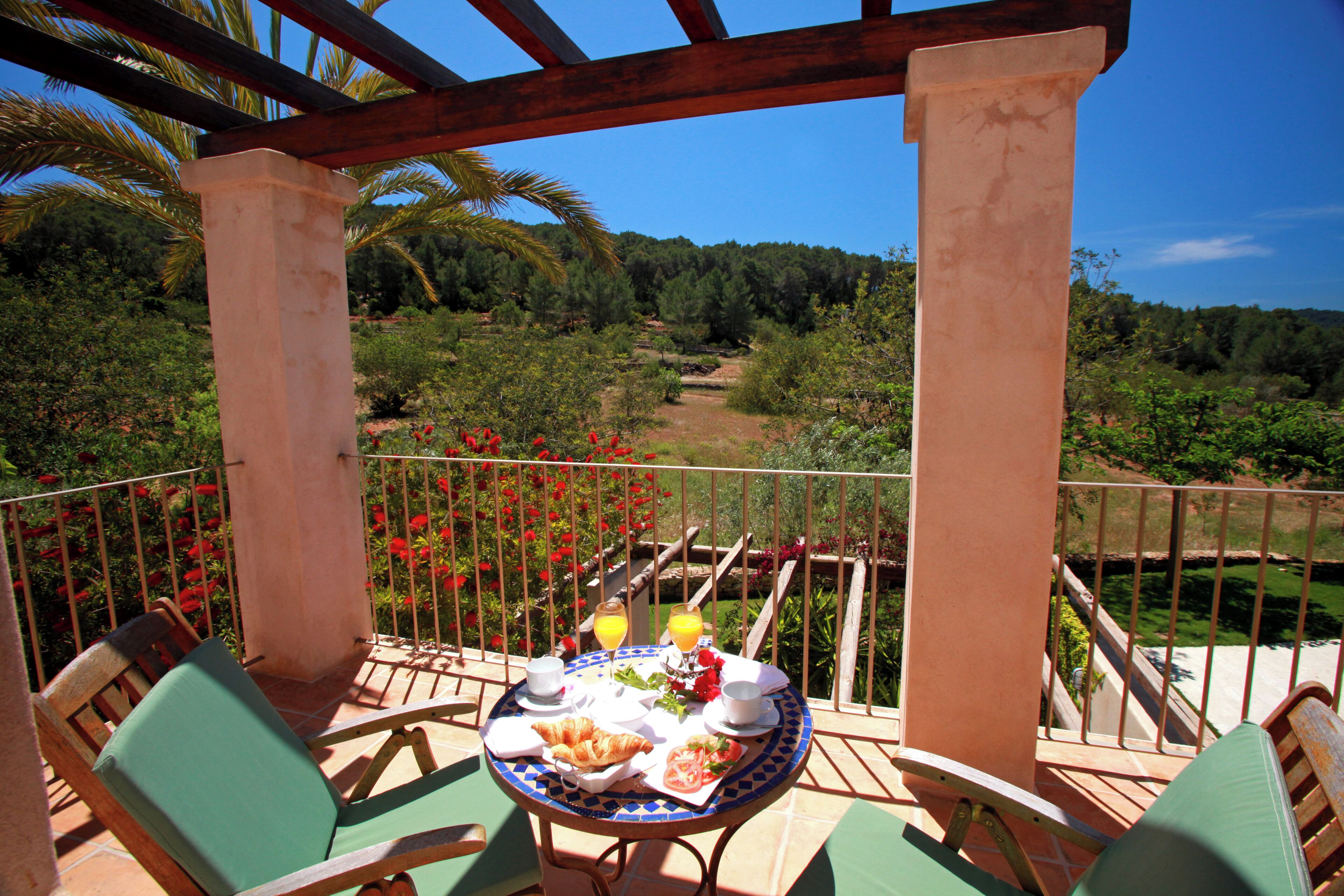 A balcony with a table set for breakfast, chairs, and a view of a forested landscape.