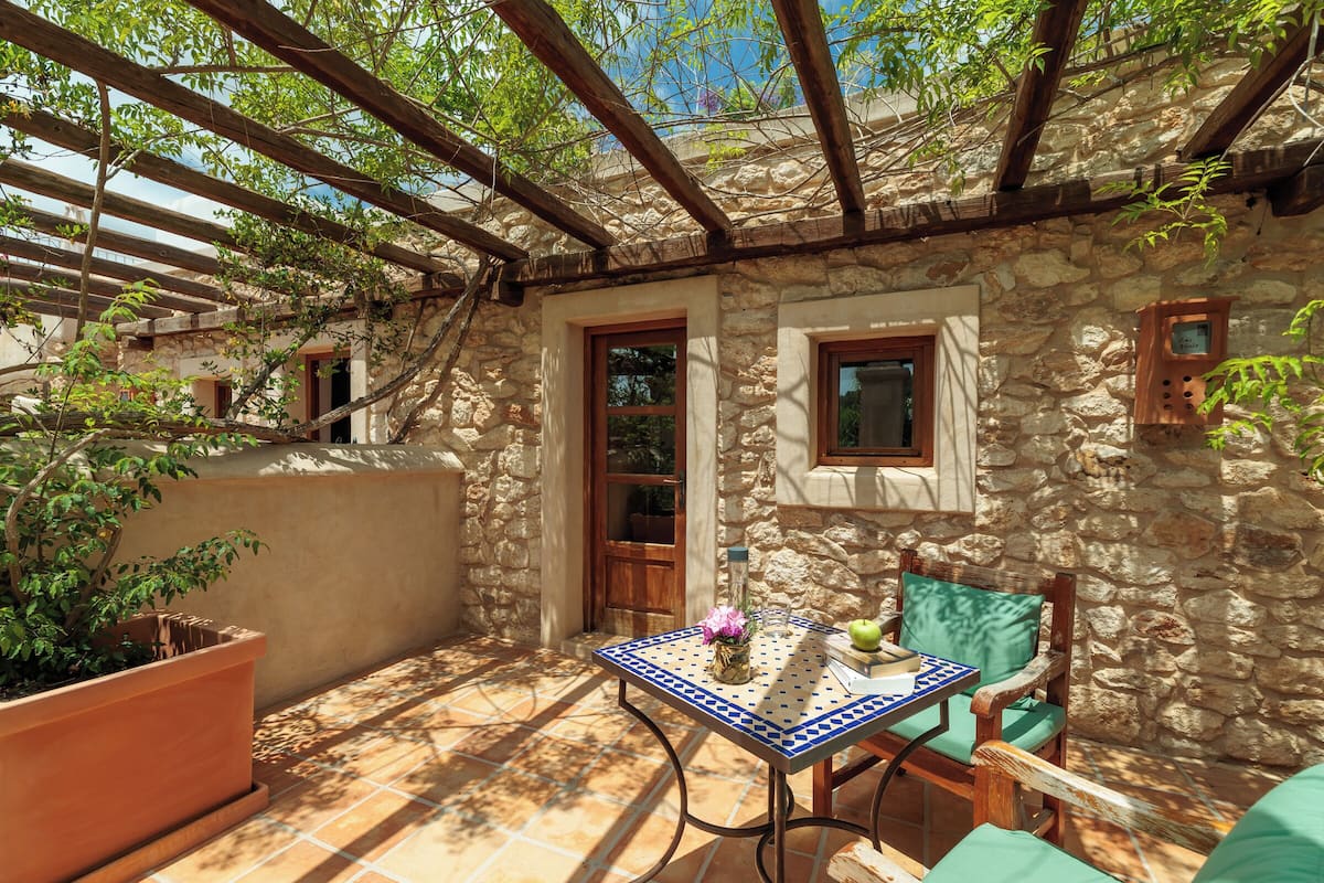 A stone-walled patio with a table and chairs, a wooden pergola, and a potted plant.