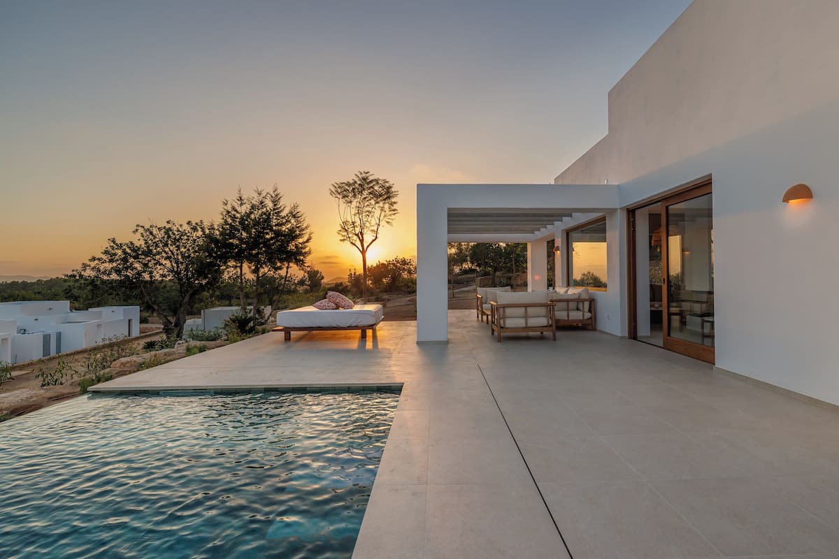 A modern outdoor pool area with a sunlit patio, a lounge chair, and a dining set.