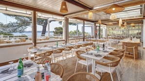 A restaurant with outdoor seating, large windows, and wicker chairs. - Belambra Clubs Presqu'île de Giens - Les Criques (Hyères)