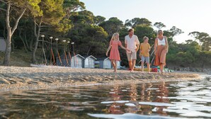 A beach with people walking, trees, and small buildings in the background. - Belambra Clubs Presqu'île de Giens - Les Criques (Hyères)