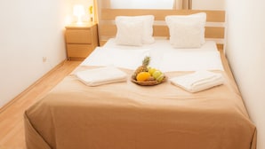 A neatly made bed with a brown bedspread, two white pillows, and a fruit basket on the bed. - Akacfa Holiday Apartments (Budapest)
