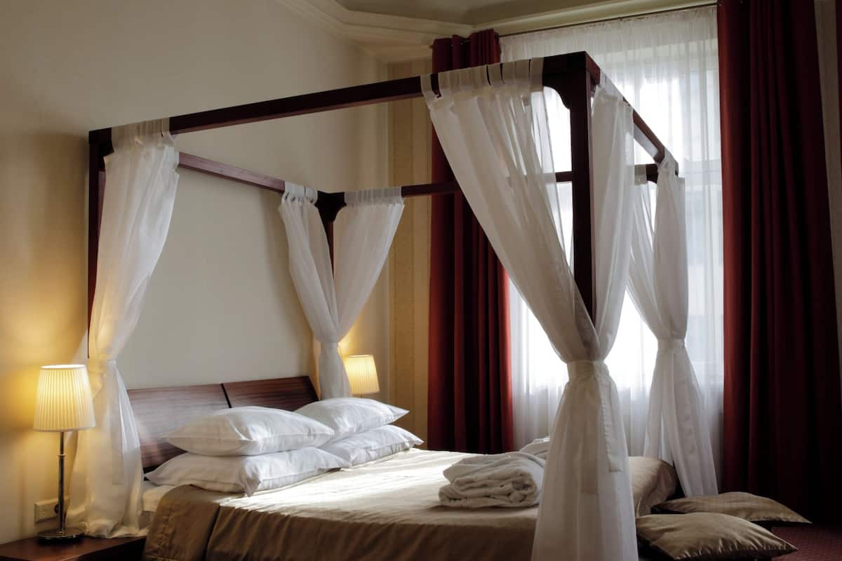 Ein Himmelsbett mit weißer Bettwäsche, einem Holz-Kopfstück und einem roten Teppichboden.