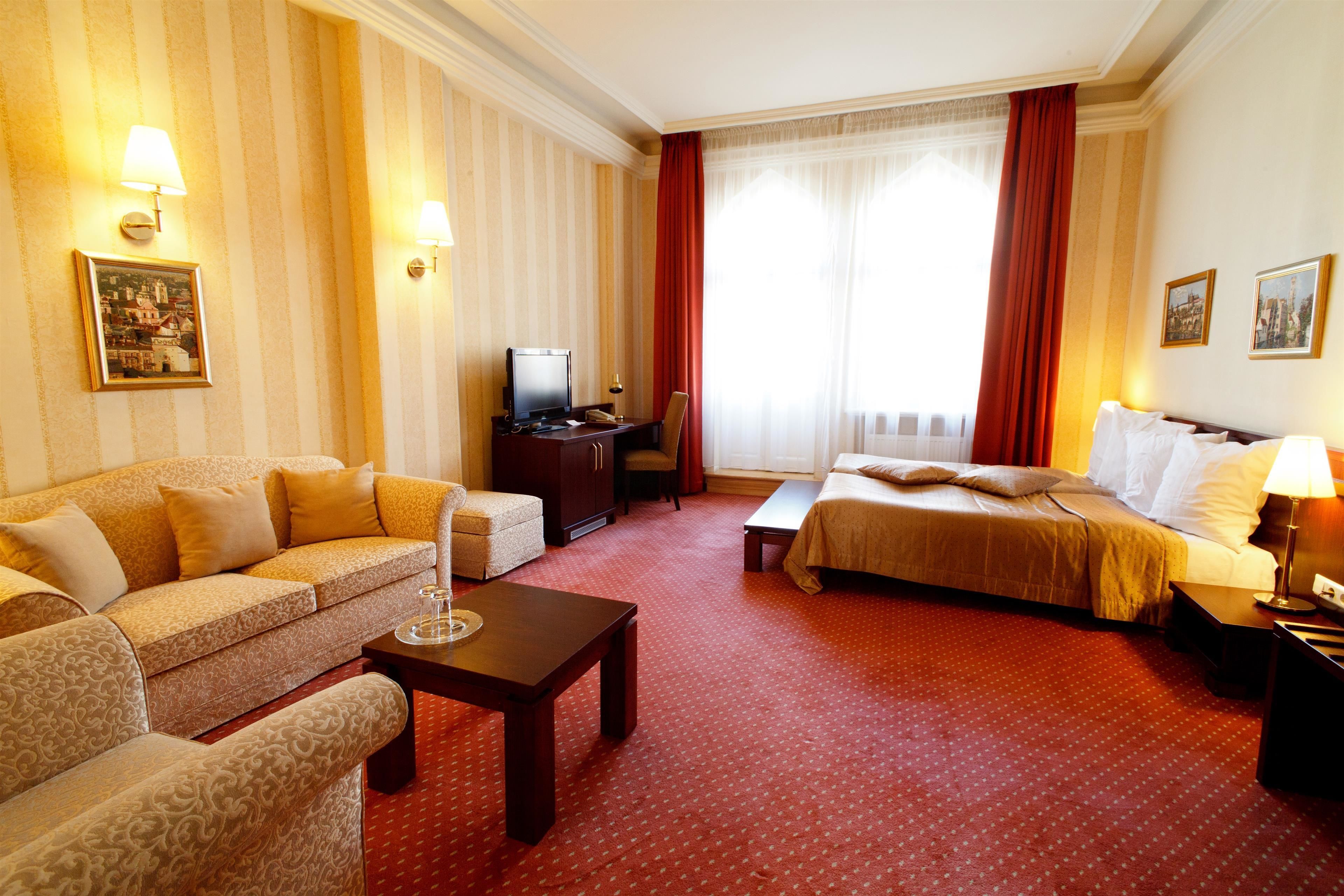 Habitación de hotel con sofá, cama, escritorio con televisor y piso cubierto de alfombra roja.