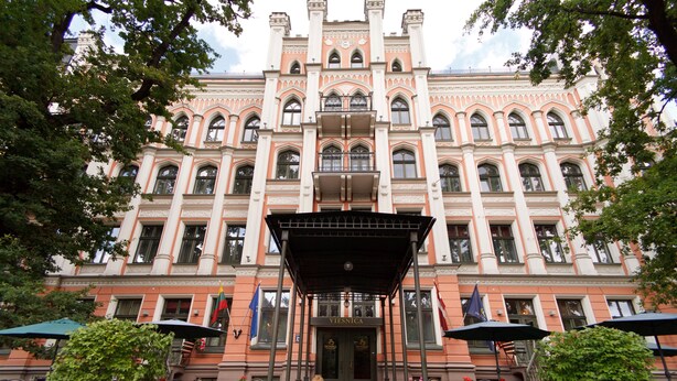 A grand building with a central entrance, multiple windows, and a covered area with chairs and umbrellas. - Monika Centrum Hotels (Riga)