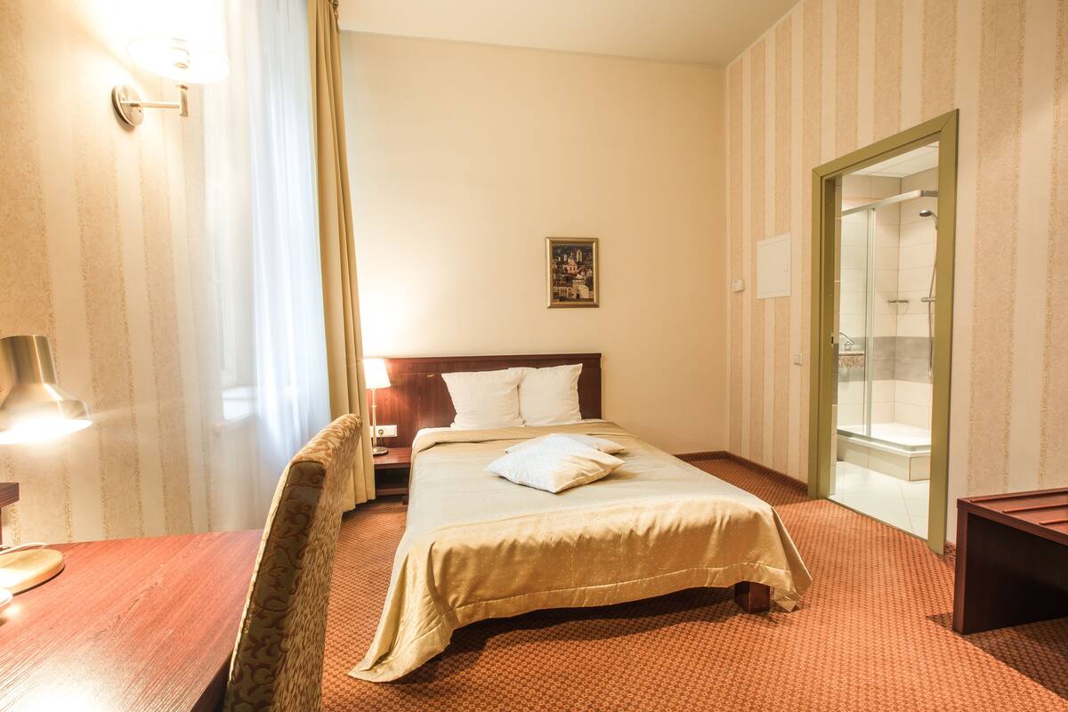 Ein Hotelzimmer mit Bett, Nachttisch, Lampe und Blick ins Badezimmer.