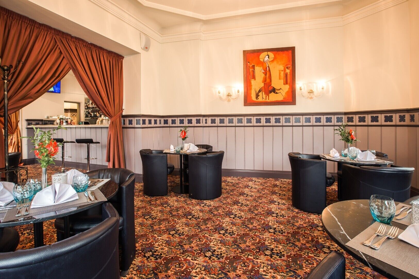 A hotel dining area with round tables, black leather chairs, and a patterned carpet.