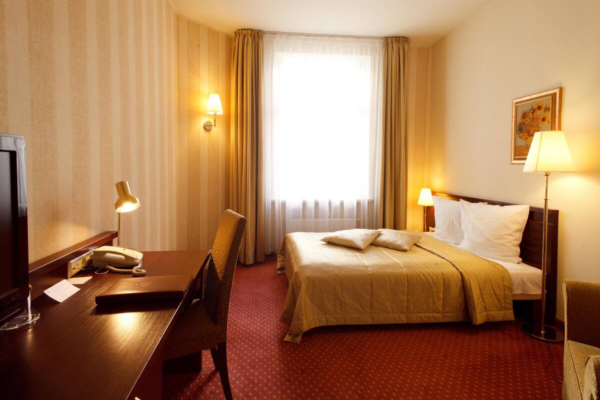 Ein Hotelzimmer mit Bett, Schreibtisch, Stuhl, Lampe und einem Fenster mit Vorhängen.