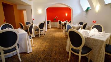 Un comedor con mesas dispuestas para seis comensales, cada una con sillas y manteles. La habitación tiene una alfombra estampada y una pared de acento roja.