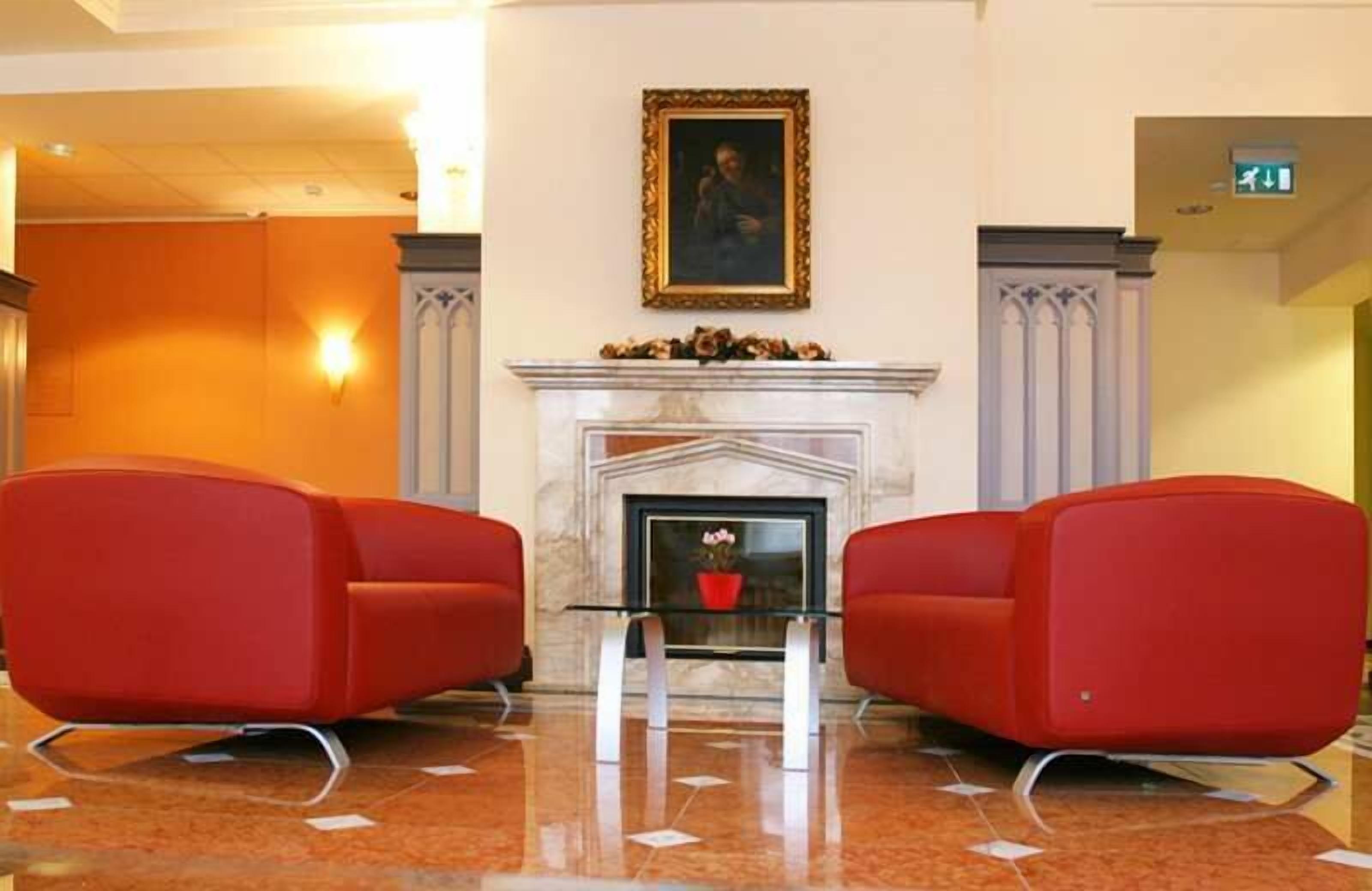 A lobby with a fireplace, red chairs, and a framed picture on the wall.