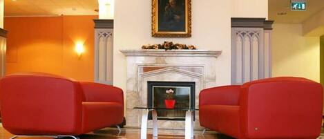 A lobby with a fireplace, red chairs, and a framed picture on the wall.