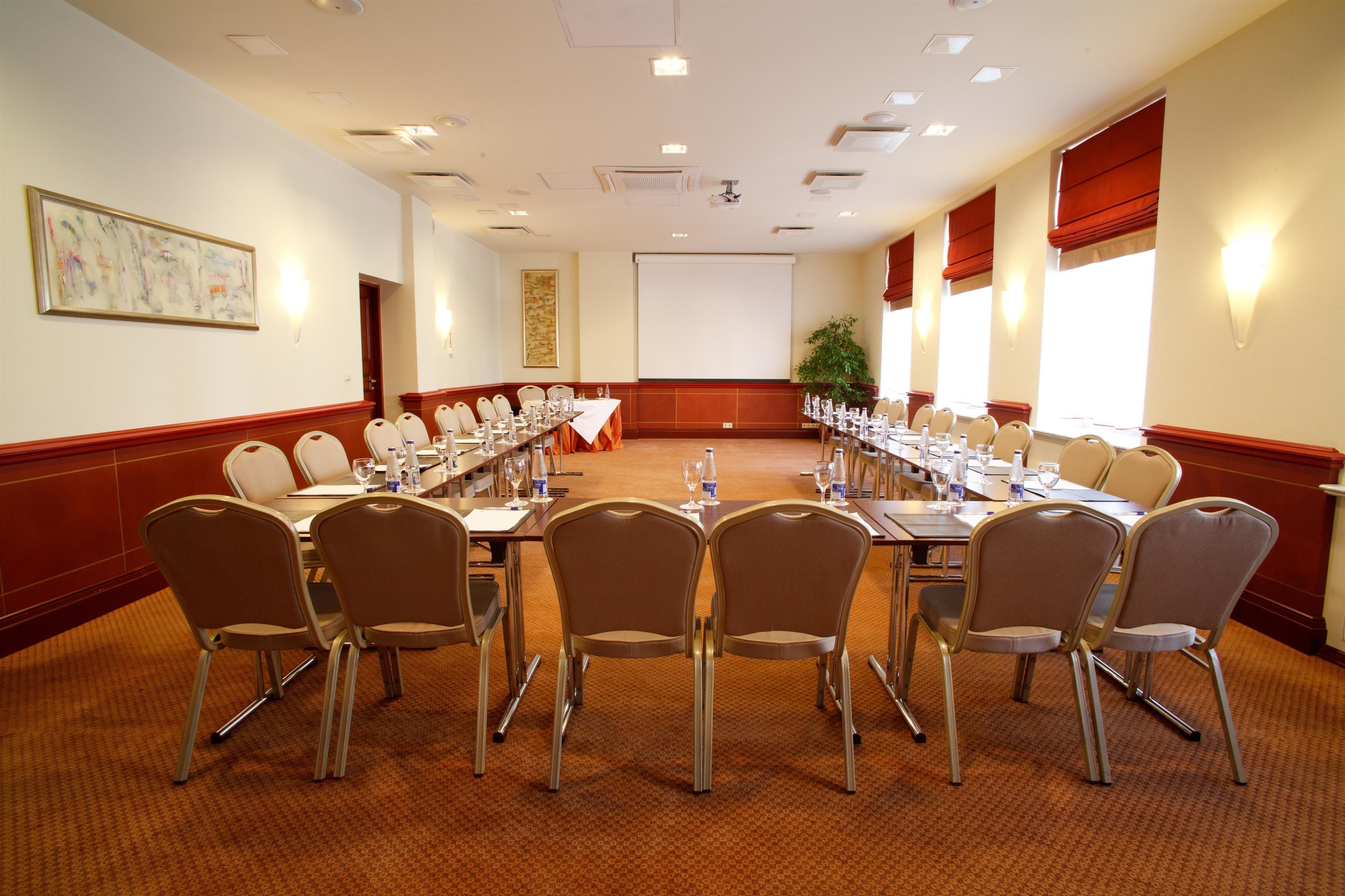 Ein Konferenzraum mit einem langen Tisch, mehreren Stühlen und einer Projektorleinwand.