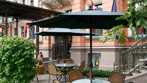 An outdoor seating area with tables and chairs, surrounded by greenery and a building with ornate architecture. - Monika Centrum Hotels (Riga)