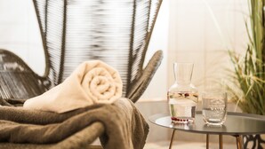 A wicker chair with a rolled towel, a glass bottle, and a glass on a small table. - Monika Centrum Hotels (Riga)