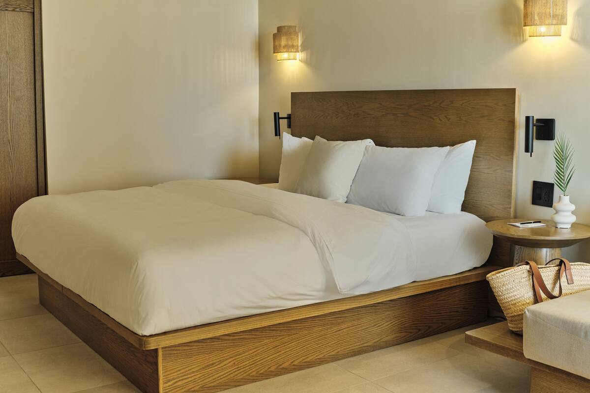 A neatly made bed with a wooden headboard, two bedside tables with lamps, and a small side table with a plant and a pen.