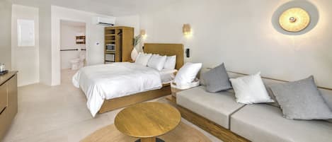 Ein modernes Schlafzimmer mit einem Bett, einem Sofa, einem runden Holztisch und einer Wandleuchte.