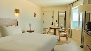 Une chambre d’hôtel avec un lit, une table à manger avec des chaises, une petite table d’appoint avec une plante, un miroir et une vue sur l’océan.