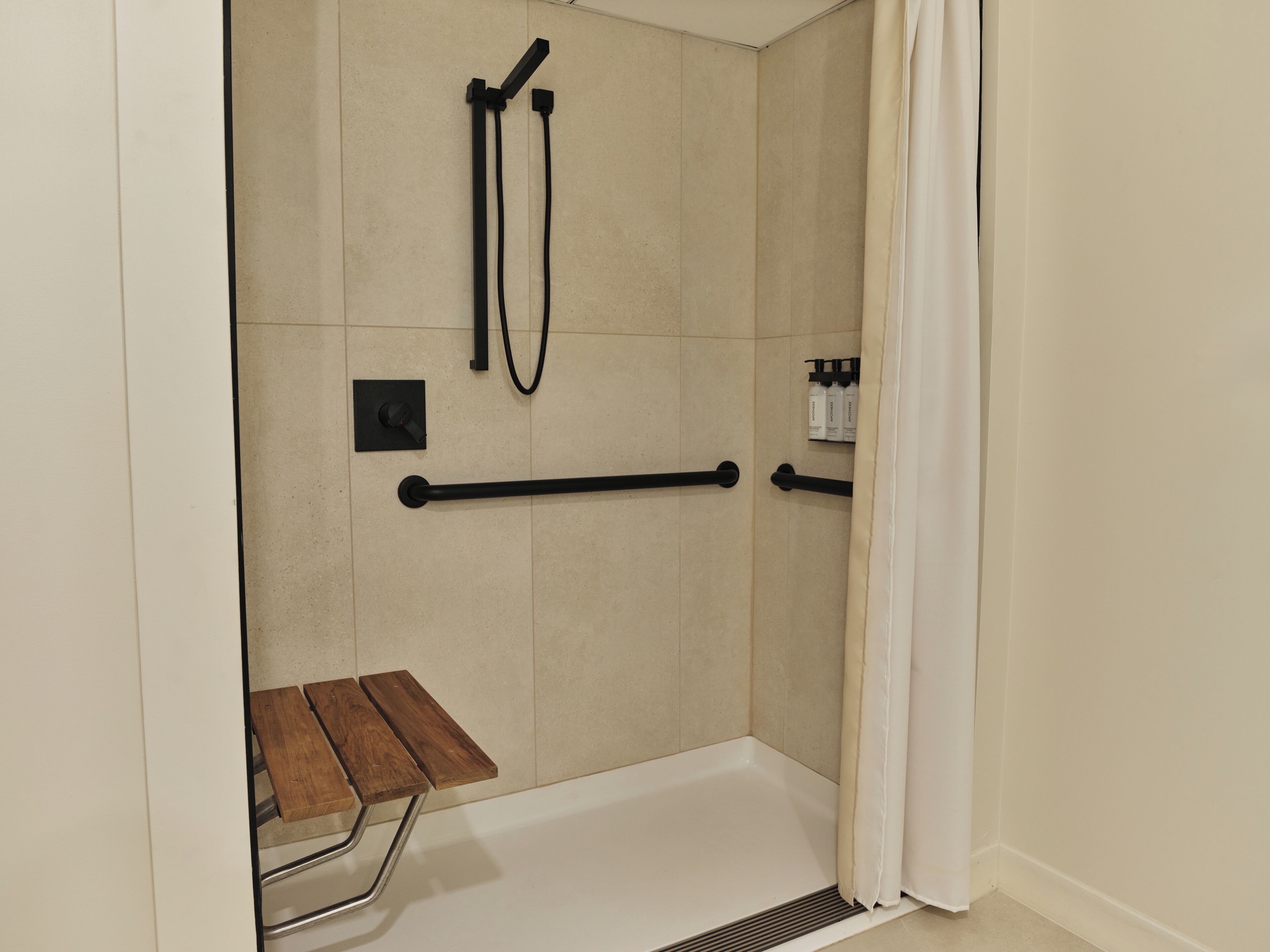 A shower area with a bench, grab bars, and a hand dryer.