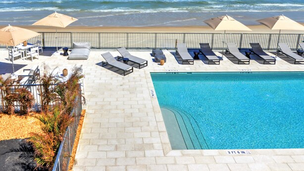 Un espace aménagé au bord de la piscine, avec des chaises longues et des parasols, offrant une vue dégagée sur l’océan, ainsi qu’une terrasse carrelée.