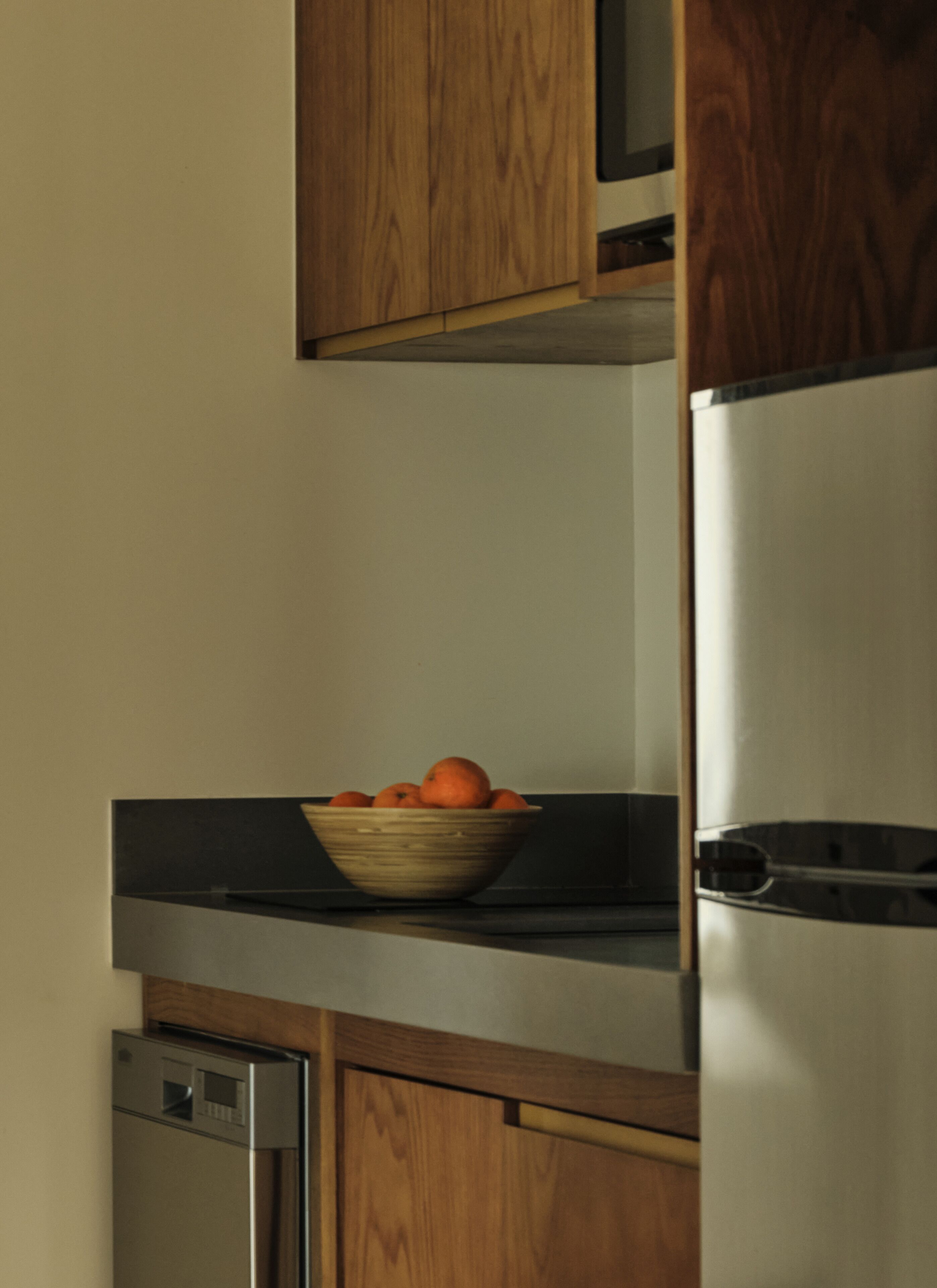 Una cocina con armarios de madera, un refrigerador de acero inoxidable y un tazón de naranjas sobre la encimera.