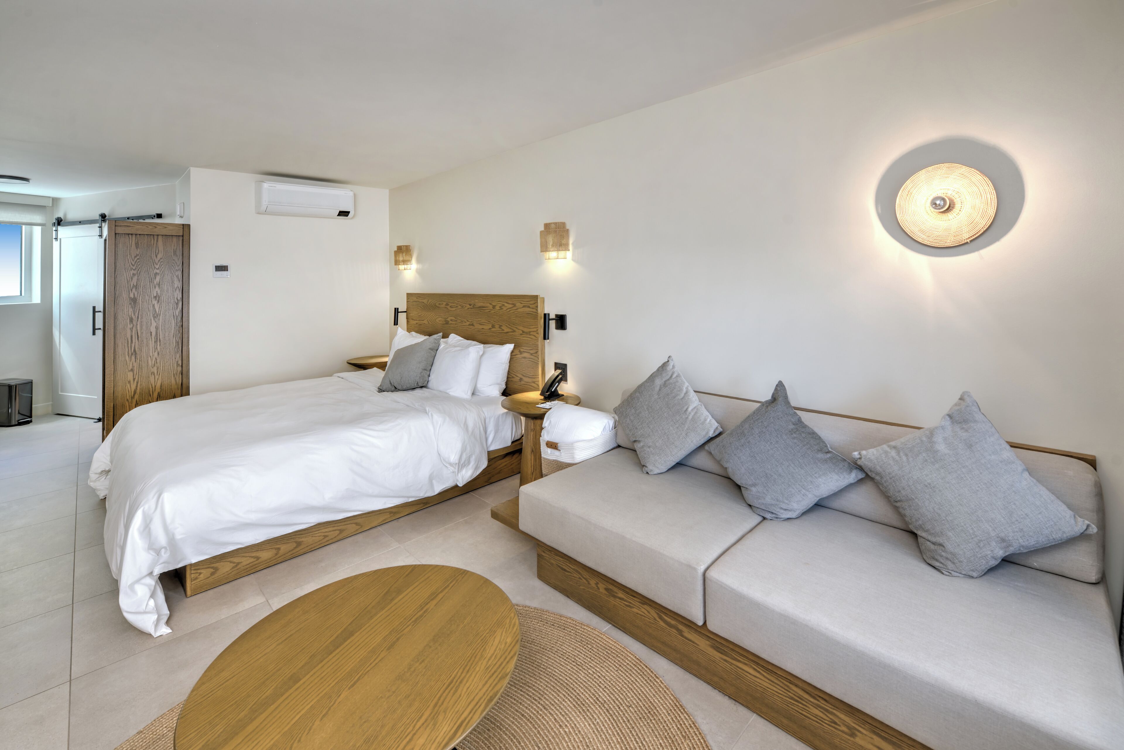A modern hotel room with a wooden bed, a sofa, and a round table.