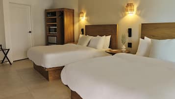 A hotel room with two beds, a wooden wardrobe, a small table, and a wall-mounted light fixture.