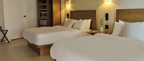 A hotel room with two beds, a wooden wardrobe, a small table, and a wall-mounted light fixture.