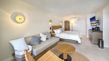 Una habitación de hotel moderna con sofá, dos camas, una mesita pequeña y un televisor montado en la pared.
