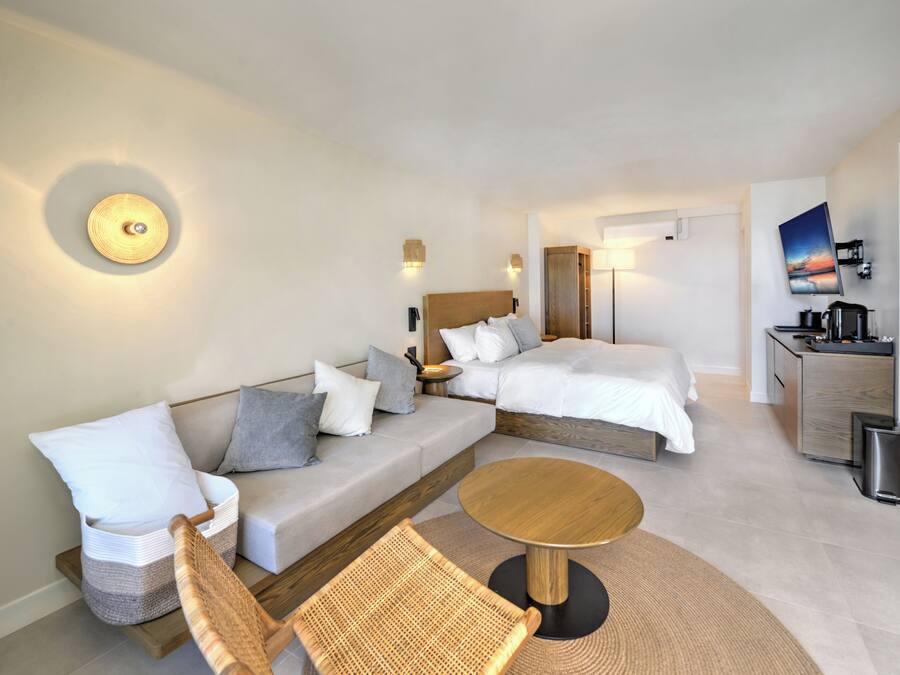 Quarto de hotel moderno com sofá, duas camas, uma mesa pequena e televisão na parede.